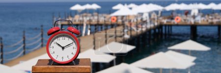 Photo for Alarm clock for ten oclock on beach with jetty and umbrellas. Summer vacation time tourism and travel to sea - Royalty Free Image