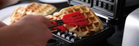 Belgian waffles in waffle iron in kitchen. hef pulls finished Belgian waffles out of oven concept