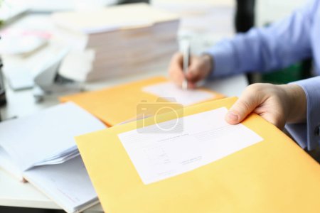 Photo for Secretary fills in address on yellow postal envelope for sending letters. Business correspondence and documentation concept - Royalty Free Image