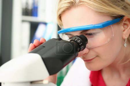 Foto de Portrait of focused female scientist looking through microscope in laboratory. Young scientist doing medical research - Imagen libre de derechos