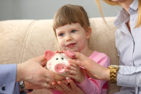 Junge Eltern und kleine Mädchen halten ein Sparschwein in der Hand. Familienhaushalt und Sparkonzept