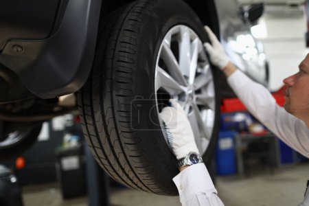 Photo for Auto mechanic in car repair shop inspects the wheels and suspension of car on lift. Auto repair shop and car maintenance - Royalty Free Image
