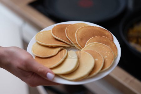 Woman hand holds plate of fresh pancakes. Cooking homemade pancakes
