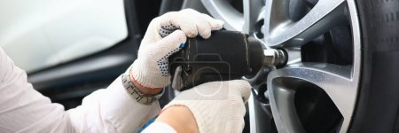 Téléchargez les photos : Garage master unscrews nuts to broken wheel of car. Tire service and auto service concept - en image libre de droit