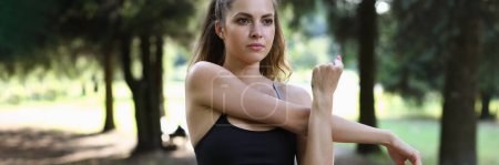 Beautiful woman stretches arms before training in park. Sports and healthy lifestyle to keep fit