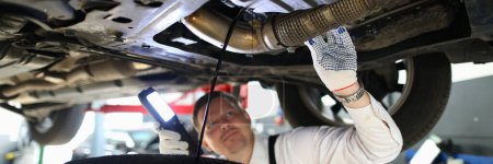 Photo for Mechanic with a lamp inspects suspension of car on lift. Auto repair and maintenance service - Royalty Free Image