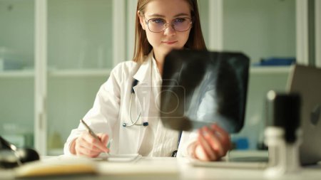 Photo for Concentrated woman surgeon traumatologist looks at x-rays examines fracture or fluorography. Doctor considers problem solving diagnostics and medical care concept - Royalty Free Image