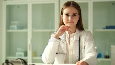 Photo for Portrait of smiling young female doctor at workplace holding eyeglasses in clinic. Nurse intern at hospital - Royalty Free Image