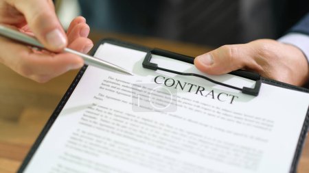 Businessman is holding tablet in hand and pointing with pen at contract documents. Man demonstrates rules written in agreement before signing