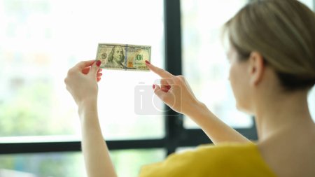 Téléchargez les photos : Un faux chèque d'argent. 100 dollars contre une fenêtre en main. Vérifiez filigrane sur le nouveau billet de cent dollars et la transparence de la monnaie américaine - en image libre de droit
