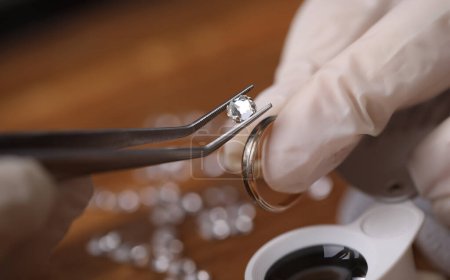 Foto de Primer plano de orfebre decorando a mano precioso anillo con hermosos diamantes. Joyero profesional usando equipo especial. concepto de producción de joyas de oro - Imagen libre de derechos