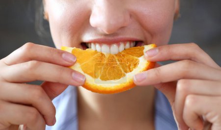 Foto de Mujer retrato sostiene en su mano rebanada de naranja picada se la come para el desayuno con su boca en concepto de cocina de dieta saludable. - Imagen libre de derechos