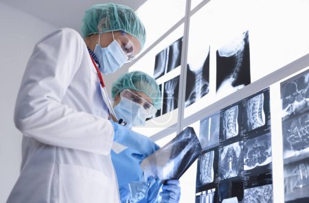 Téléchargez les photos : Deux travailleurs médicaux portant des masques médicaux de protection, des gants et des lunettes examinent les rayons X. Concept d'examen des organes internes - en image libre de droit