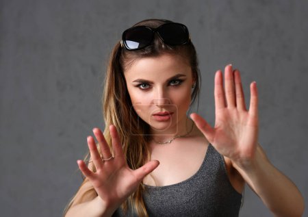 Photo for Beautiful young brunette girl wearing sunglasses protect herself with arms portrait at grey background. Fortune teller mime spell magic calm down say no concept - Royalty Free Image