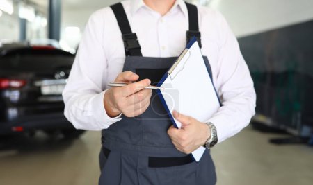 Photo for Focus on smart man standing in modern car maintenance garage and holding important paper folder with information about different autos. Machinery repairman concept - Royalty Free Image