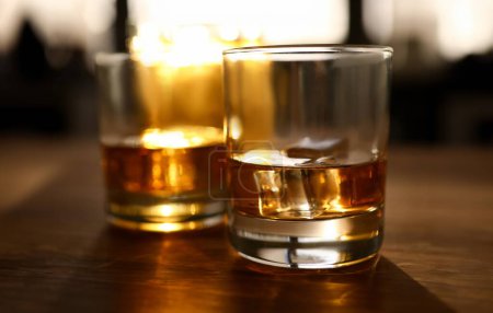 Téléchargez les photos : Focus sur les verres de whisky ou de bourbon avec glaçons. Verres de délicieuses boissons sur table en bois. Célébration et concept relax. Fond flou - en image libre de droit