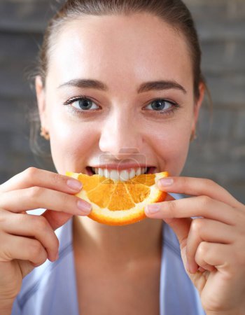 Foto de Mujer retrato sostiene en su mano una rebanada de naranja picada se la come para el desayuno con la boca en el concepto de cocina de una dieta saludable
. - Imagen libre de derechos