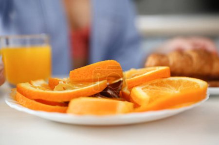 Foto de Rebanadas de naranja en un plato en una mesa de cocina en el fondo un vaso borroso de jugo - Imagen libre de derechos