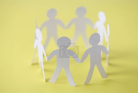Téléchargez les photos : Couper les gens en papier formant un cercle syndical sur fond jaune. Travail d'équipe et réalisation d'un concept commun de réussite - en image libre de droit