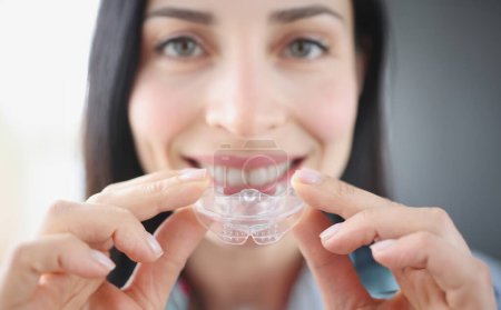Une femme souriante tient un protège-dents en plastique transparent pour redresser les dents. Correction des morsures et bruxisme concept