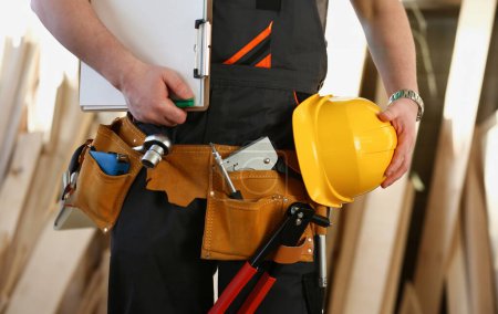Téléchargez les photos : Homme à tout faire avec les mains sur la taille et la ceinture d'outils avec des outils de construction sur fond de bois. Outils de bricolage et concept de travail manuel - en image libre de droit