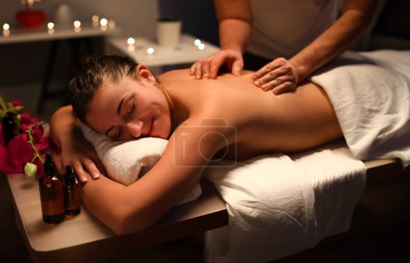 Téléchargez les photos : Masseur femme souriante faisant massage du dos au centre de spa. Avantages du massage thérapeutique pour le dos et la colonne vertébrale concept - en image libre de droit