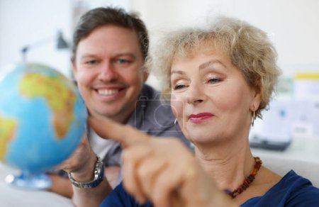 Photo for An elderly woman and young man looking at globe. Parents and children traveling together concept - Royalty Free Image