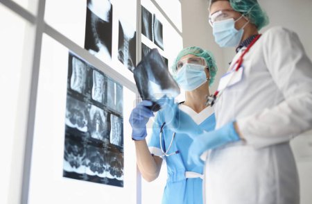 Téléchargez les photos : Deux médecins portant des masques de protection médicale examinent les radiographies. Lésion pulmonaire dans le concept de coronavirus - en image libre de droit
