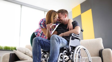 Téléchargez les photos : Joyeuse femme et homme en fauteuil roulant avec test de grossesse. Premières émotions du concept de futurs parents - en image libre de droit