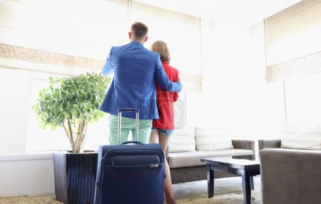 Photo for Portrait of couple dressed in suits, suitcase behind, enjoy view out of window, wait for flight, short delay, airport terminal. Trip concept. Copy space - Royalty Free Image