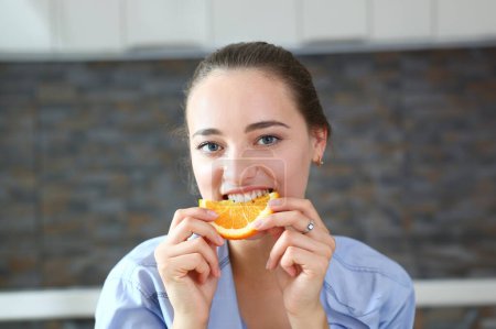 Foto de Mujer retrato sostiene en su mano una rebanada de naranja picada se la come para el desayuno con la boca. En el concepto de cocina de una dieta saludable. - Imagen libre de derechos