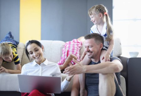 Photo for Man and woman and their children are smiling and laughing while sitting on floor and looking at laptop. Family time together concept - Royalty Free Image