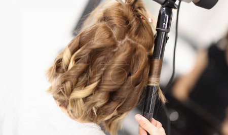 Téléchargez les photos : Coiffeur fait des boucles sur les cheveux des femmes avec du fer à friser. Salon de beauté services concept - en image libre de droit
