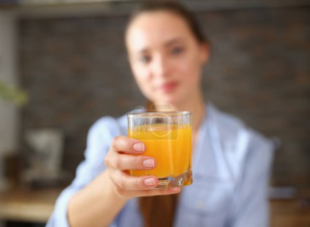 Photo for Young beautiful attractive girl in pajamas in the kitchen drinking orange juice holding a glass in her hand - Royalty Free Image