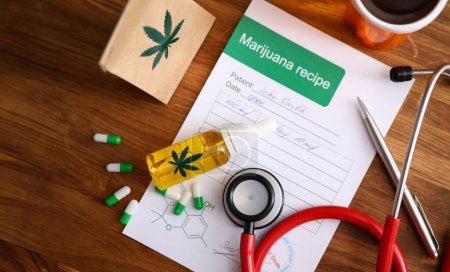 Draufsicht auf Papier Marihuana Rezept. Auf einem Holztisch liegen bunte Pillen und Cannabinoidöl. rotes medizinisches Stethoskop Medizin und Gesundheitskonzept