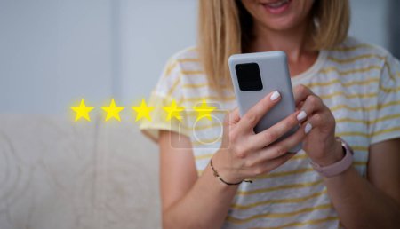 Frau hält Handy in der Hand und gibt fünf Sterne für die Qualität der Dienstleistungen Nahaufnahme. Online-Bewertungskonzept