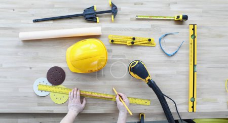 Photo for Top view of engineer markup for construction site. Working equipment on table. Foreman hands holding ruler and pencil. Yellow helmet of desk. Renovation concept - Royalty Free Image