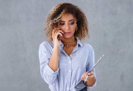 Photo for Beautiful black woman portrait. Holds a clipboard and talks on the phone fashion style curly hair with white locks eye view of the camera - Royalty Free Image