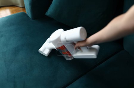 Photo for Hand vacuums upholstered furniture in apartment. Design features and unique advantages household appliances for dry cleaning in apartment. Tool sucks in dust and small debris on couch - Royalty Free Image