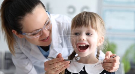 Woman dentist examines teeth in clinic at child. Doctor will monitor home dental hygiene. Dentist will conduct additional training, home hygiene. Guarantee for fillings before tooth changes