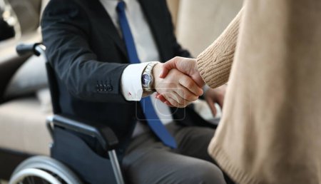 Close-up view of co-workers shaking hands. Businesswoman and disabled colleague on wheelchair. Business meeting and negotiations. Adaptation of people with disabilities in society concept