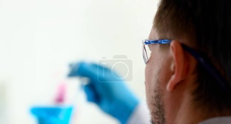 A male chemist holds test tube of glass in his hand overflows a liquid solution of potassium permanganate conducts an analysis reaction takes various versions of reagents using chemical manufacturing.