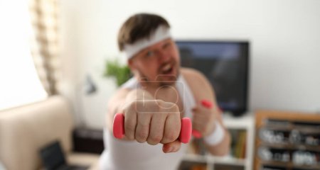 Photo for Young attractive man engaged in fitness at home holding dumbbell in hand trying to fight excess weight and loss - Royalty Free Image