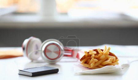Papas fritas con auriculares acostados en la mesa en la oficina durante la pausa para el almuerzo concepto de entrega de alimentos
