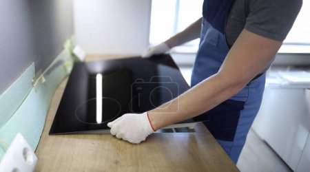 Nahaufnahme vom professionellen Handwerker, der einen Kochherd einrichtet. Männchen in weißen Schutzhandschuhen in der Küche. Bewegender Tag in neuer Wohnung. Sanierungs- und Reparaturkonzept