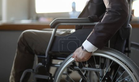 Großaufnahme eines behinderten Mannes im Rollstuhl im Büro, der einen vorzeigbaren Anzug trägt. Anpassung von Menschen mit Behinderungen an die Gesellschaft. Erholungs- und Gesundheitskonzept