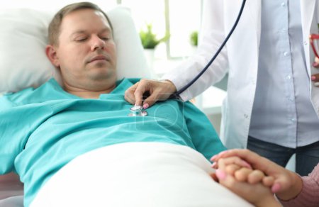 Sick man lies on bed in clinic, doctor examines. Intensity healing process. Doctor determines need for diagnostic tests. Further health monitoring. Highly qualified professional medical staff