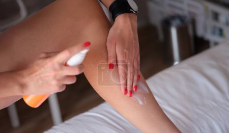Foto de Chica utiliza spray y se aplica protector solar en la pierna. Protección y cuidado de la piel en verano - Imagen libre de derechos