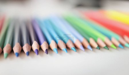Many sharp multicolored pencils lying over colors of rainbow closeup background. School of fine arts concept