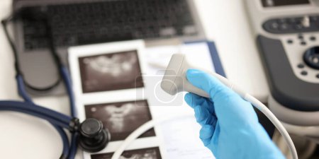Doctor holding ultrasound probe against background of pictures and medical documents closeup. Instrumental diagnostics in medicine concept